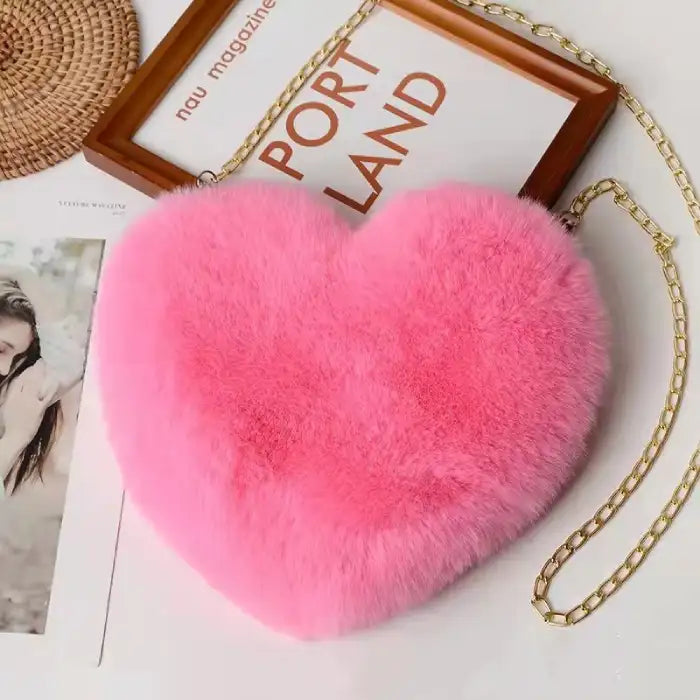 Bright pink heart shoulder bag with fluffy texture and gold chain strap on a magazine setup.