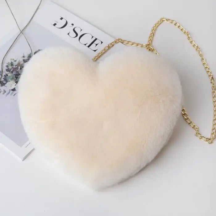 Cream-colored plush heart shoulder bag with gold chain on a minimal white setup.