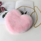 Light pink heart-shaped plush shoulder bag with gold chain on floral book background.