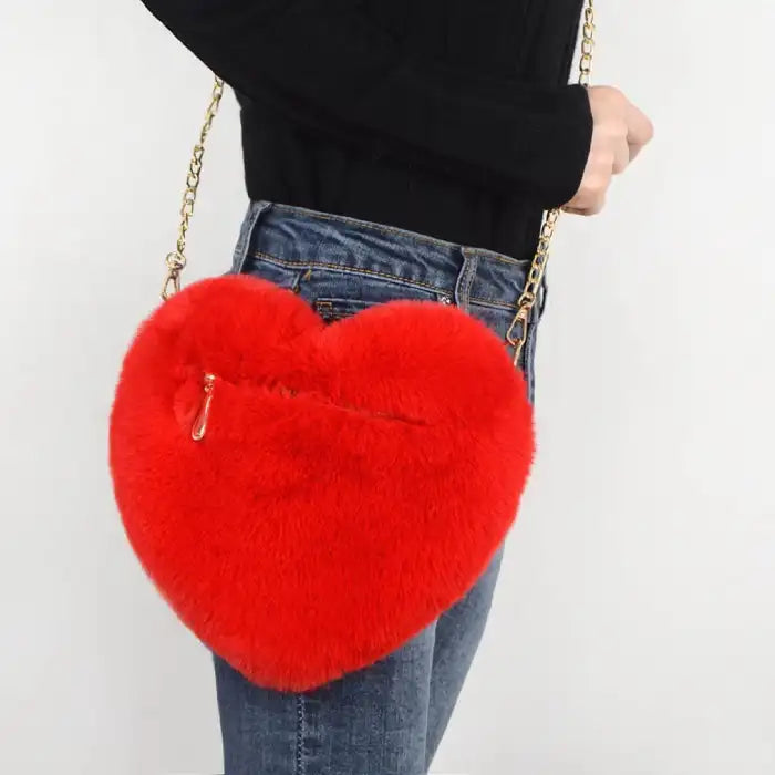 Heart shoulder bag in bold red plush with visible zipper and gold chain strap.