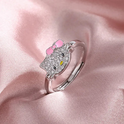 Hello kitty jewelry set ring with crystal face and pink bow displayed on soft pink satin fabric.