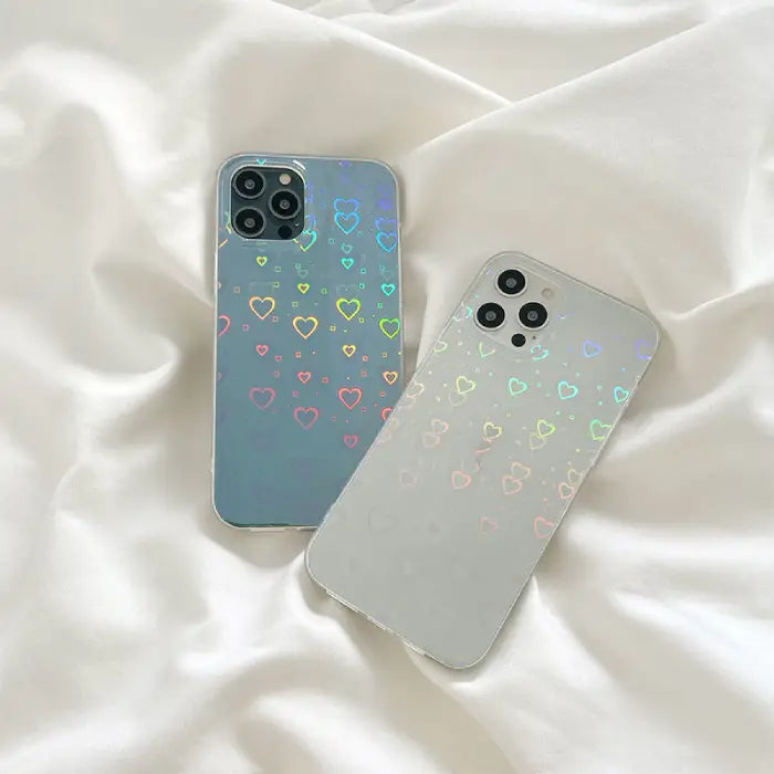 Two holographic heart design phone cases on white fabric, showcasing stylish protective phone accessories.