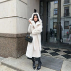 Hooded long plush coat worn outdoors with black boots and handbag.