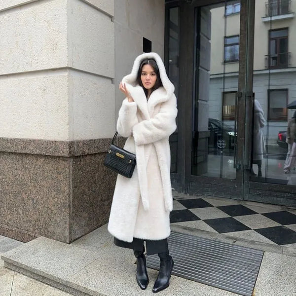 Hooded long plush coat worn outdoors with black boots and handbag.