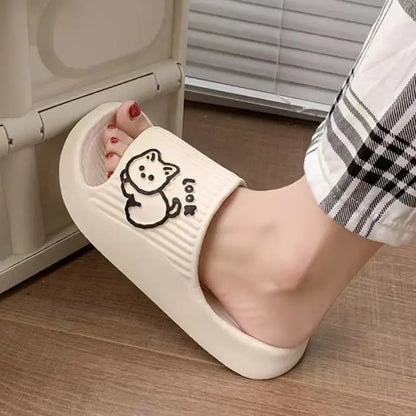 Single white indoor slide with cartoon cat design shown on foot against wooden flooring and plaid fabric