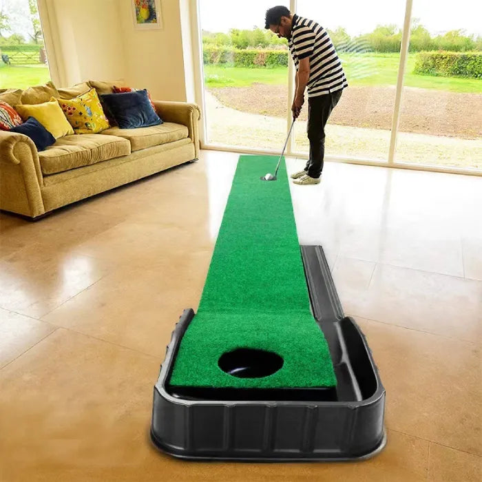 Man using indoor putting green in a living room setting with natural light and couch nearby