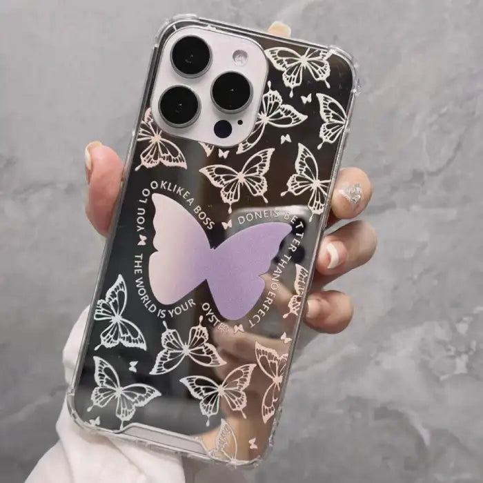 iPhone 15 case with mirror background featuring white butterfly patterns and central purple butterfly accent with motivational text