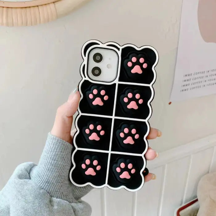 iPhone cute case featuring black background with pink 3D cat paw prints arranged in grid pattern with white scalloped border