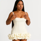 ruffle hem dress in ivory white featuring straight neckline, thin straps and voluminous gathered bottom detail in studio setting