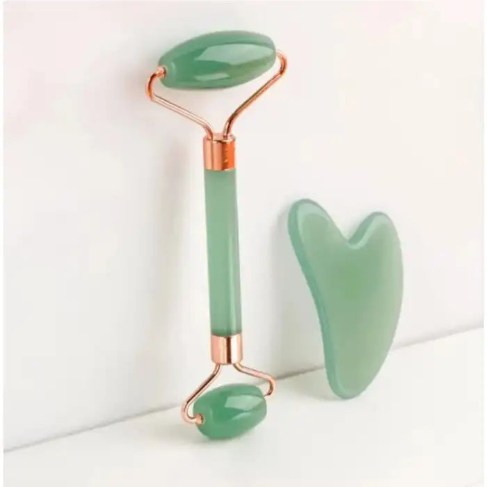 Jade roller and gua sha set in green stone with rose gold accents placed on white background