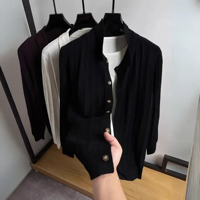  Black knit cardigan with wooden buttons displayed on hanger, hand holding the sleeve cuff.