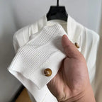 Close-up of knit cardigan sleeve in white showing textured knit pattern and wooden button detail.