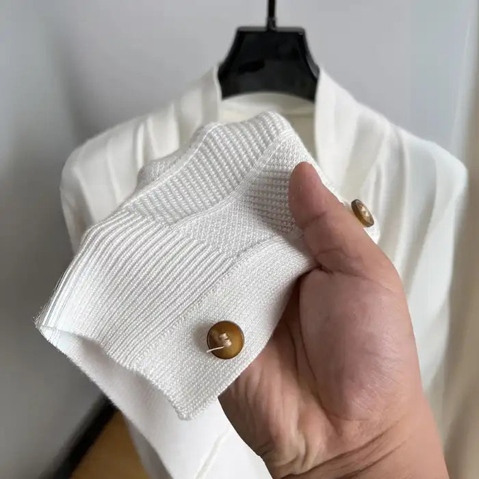 Close-up of knit cardigan sleeve in white showing textured knit pattern and wooden button detail.