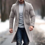 Lapel trench coat in beige worn over sweater and jeans in a stylish snowy winter park setting.