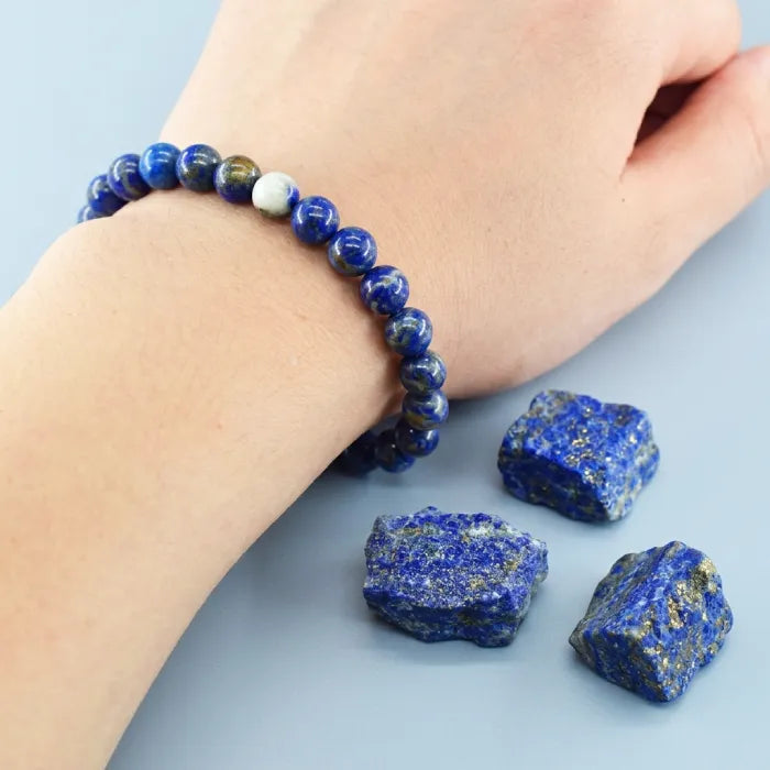 Lapis lazuli bracelet worn on wrist with raw stones nearby, polished gemstone bead jewelry for stylish everyday wear