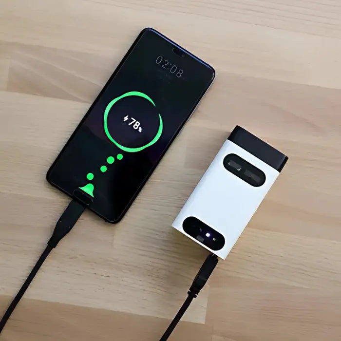 Laser keyboard charging via USB cable connected to smartphone on light wood surface.