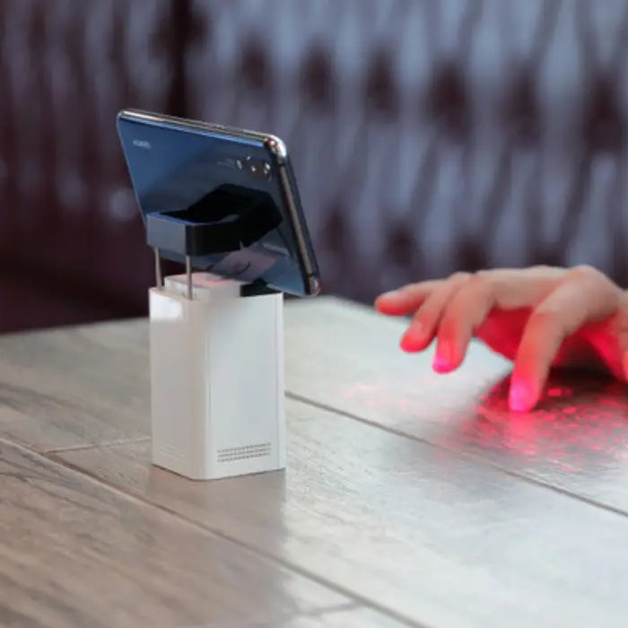 Laser keyboard for smartphone projecting red keyboard with hand typing on wood table.