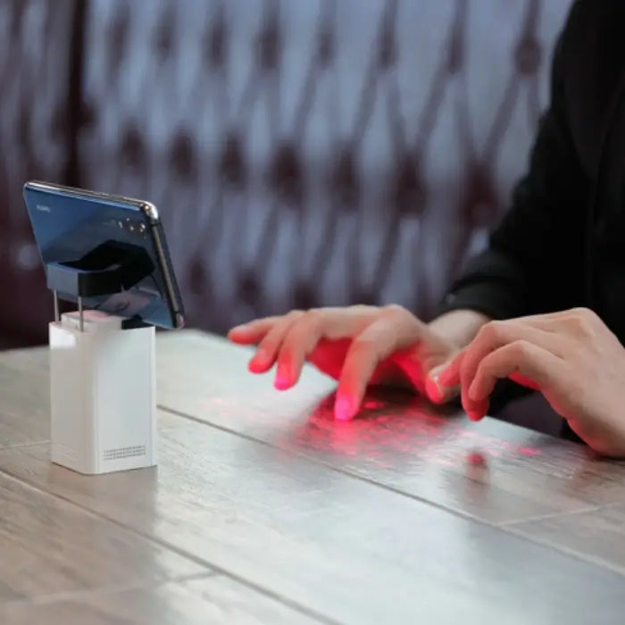 Laser projection keyboard connected to laptop with red keyboard projected on desk surface.