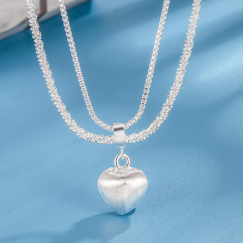 layered silver heart necklace with shiny double chains and brushed silver heart pendant shown in front display