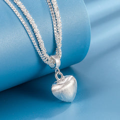 layered silver heart necklace with textured heart pendant resting on rolled blue backdrop for product display