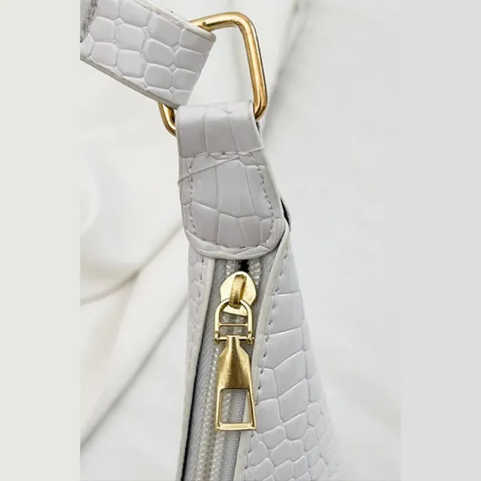 Close-up of white croc-embossed leather bag strap with gold-tone hardware and zipper pull