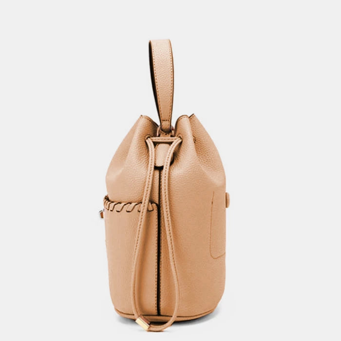 Structured tan leather bucket bag showing drawstring closure system and quality stitching details