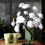 LED tree lamp with white artificial roses on a black stand, styled with cups and wine bottle in background.