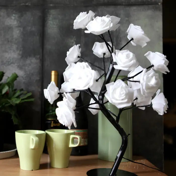 LED tree lamp with white artificial roses on a black stand, styled with cups and wine bottle in background.