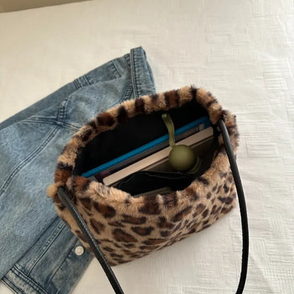 Open leopard print faux fur bag with visible contents, paired with blue denim jacket on a white surface.