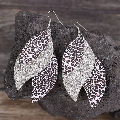 A pair of layered leaf-shaped earrings with leopard print and glitter accents displayed on a gray textured background.