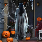 Life size Halloween prop of ghost woman with flowing white gown walking up decorated porch at night.