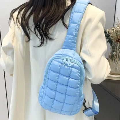 Light blue quilted sling bag worn with white coat, showcasing trendy winter fashion accessory