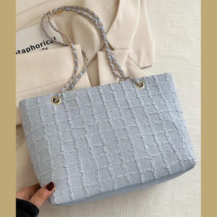 Light blue textured tote bag with chain strap on cream background