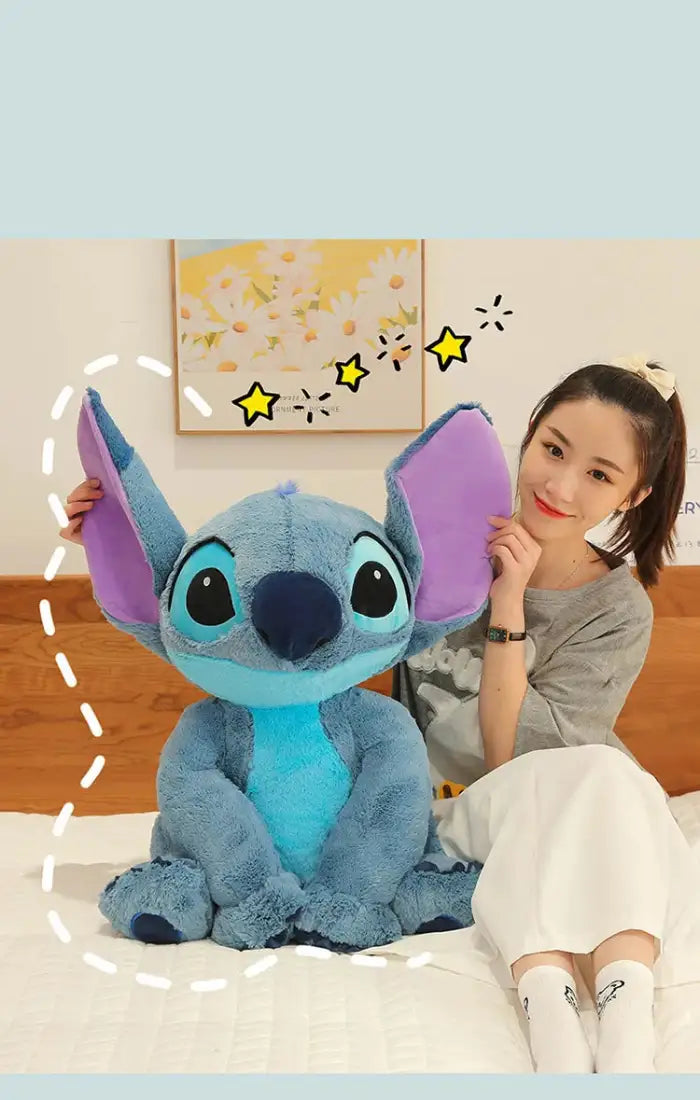 lilo and Stitch big plush toy sitting beside smiling woman on bed under flower wall art