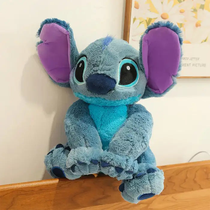 lilo and stitch blue plush doll with purple ears sitting on wooden bed frame near wall art
