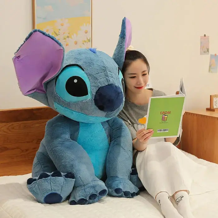 lilo and Stitch large plush sitting on bed with woman reading beside it