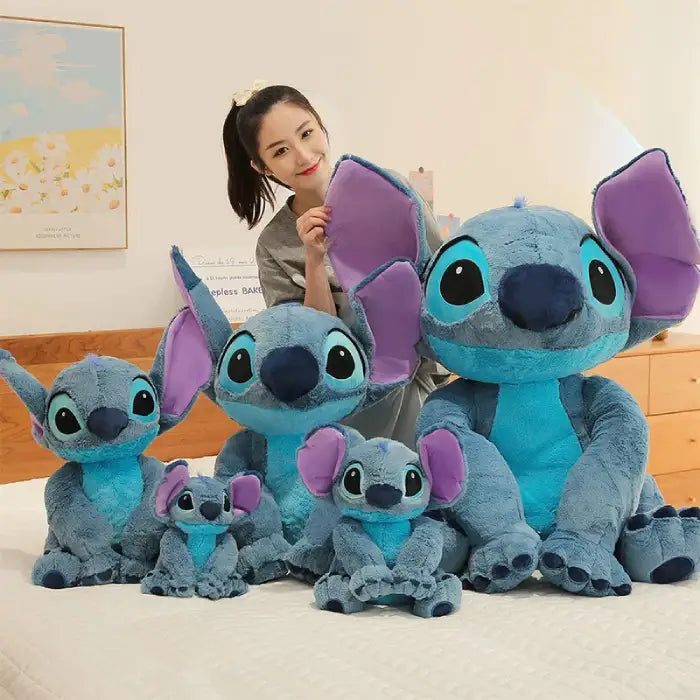 lilo & Stitch plush toy collection in various sizes displayed on bed with smiling woman