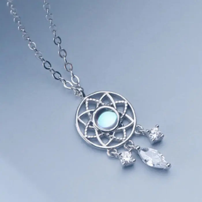 Luminous dreamcatcher silver pendant necklace with crystal charms displayed on a light blue background.