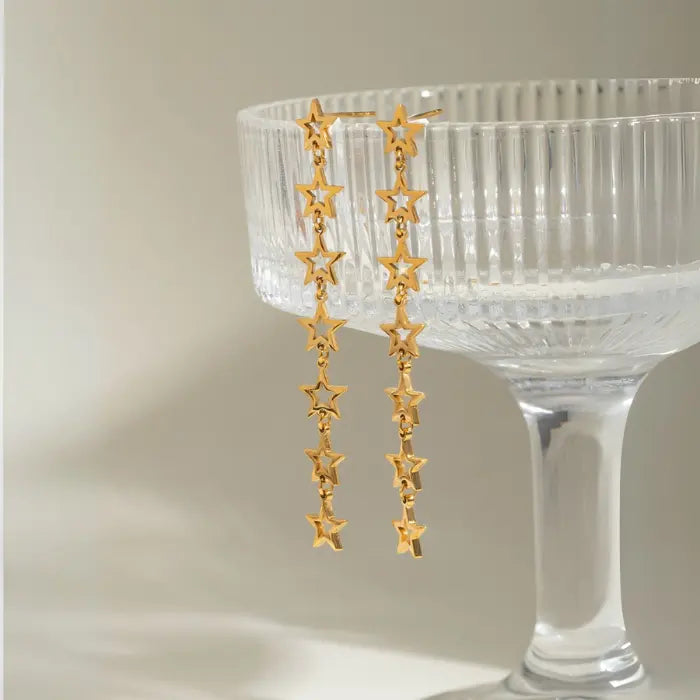 Gold star drop earrings displayed against vintage crystal champagne glass