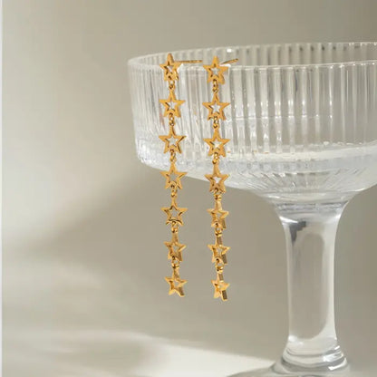 Gold star drop earrings displayed against vintage crystal champagne glass