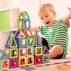 Magnetic building blocks stacked by excited boy into a tall, colorful geometric structure on a rug.