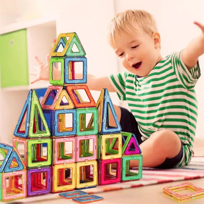 Magnetic building blocks stacked by excited boy into a tall, colorful geometric structure on a rug.