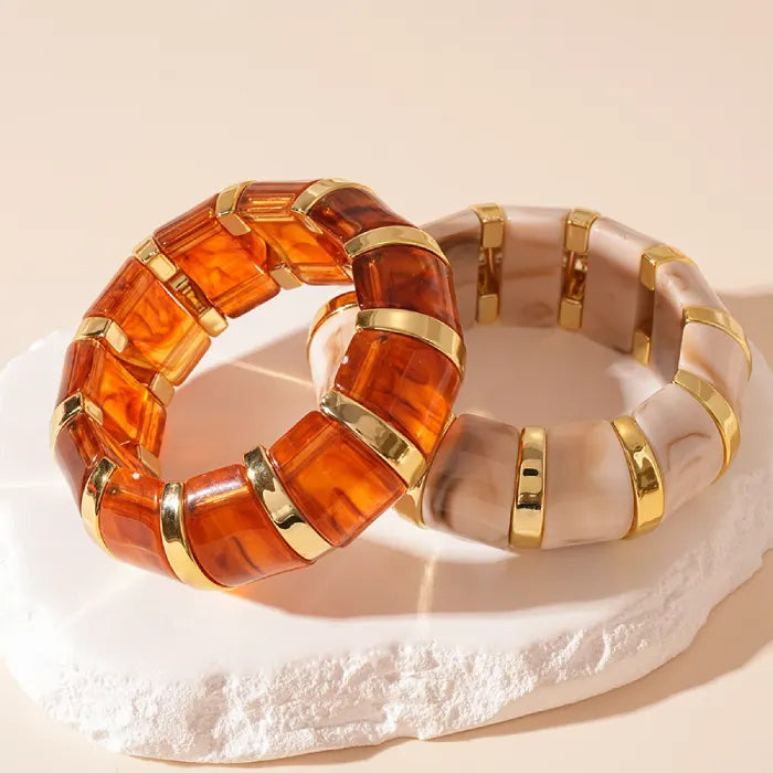 marbled acrylic bracelets in amber and beige colors with gold trim displayed on textured white platform