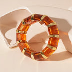 marbled acrylic bracelet in deep amber color with gold accents positioned against sculpted beige backdrop