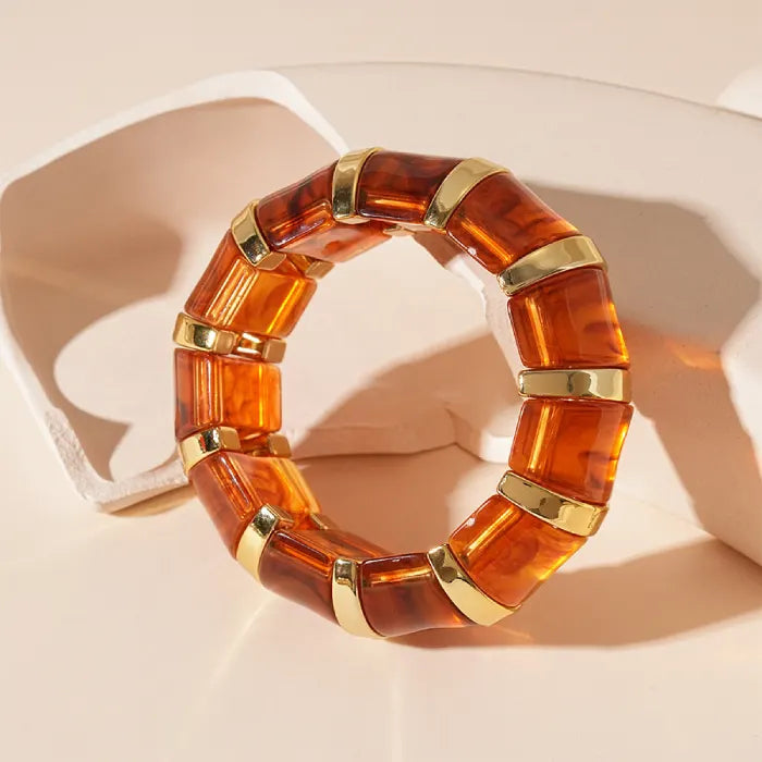 marbled acrylic bracelet in deep amber color with gold accents positioned against sculpted beige backdrop