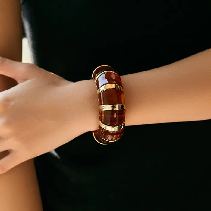 marbled acrylic bracelets in translucent wooden brown with gold accents worn on model’s arm against white outfit