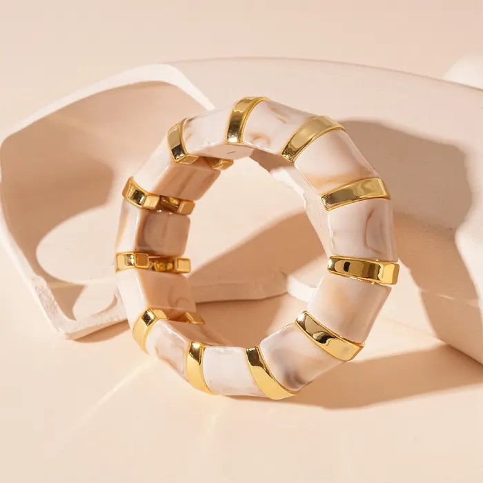 marbled acrylic bracelet in cream tone with gold detailing displayed against minimal beige background
