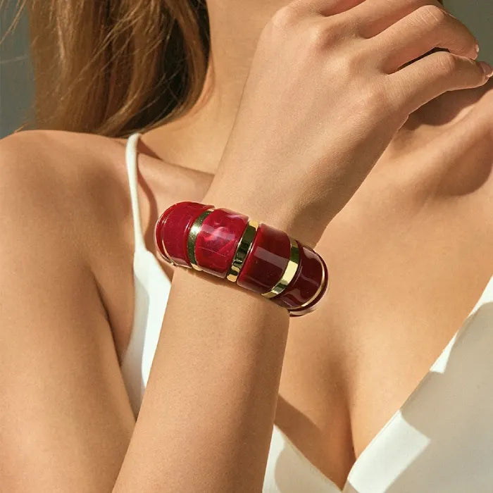 marbled acrylic bracelets in translucent dark red with gold accents worn on model’s arm against white outfit