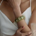 marbled acrylic bracelets in translucent green with gold accents worn on model’s arm against white outfit