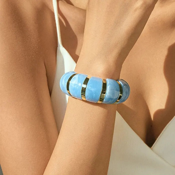 marbled acrylic bracelets in translucent light blue with gold accents worn on model’s arm against white outfit
